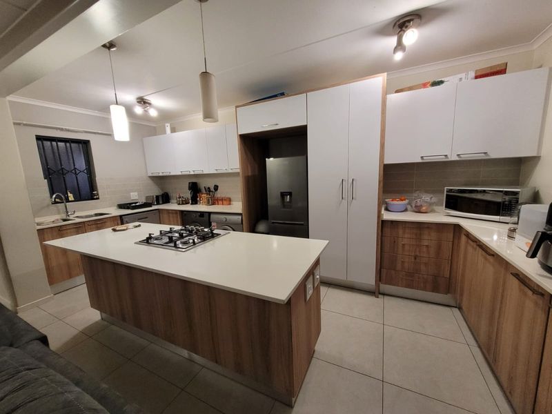 Modern kitchen featuring a central island with a gas hob, stone countertops, ample built-in cabinetry, and tiled flooring.