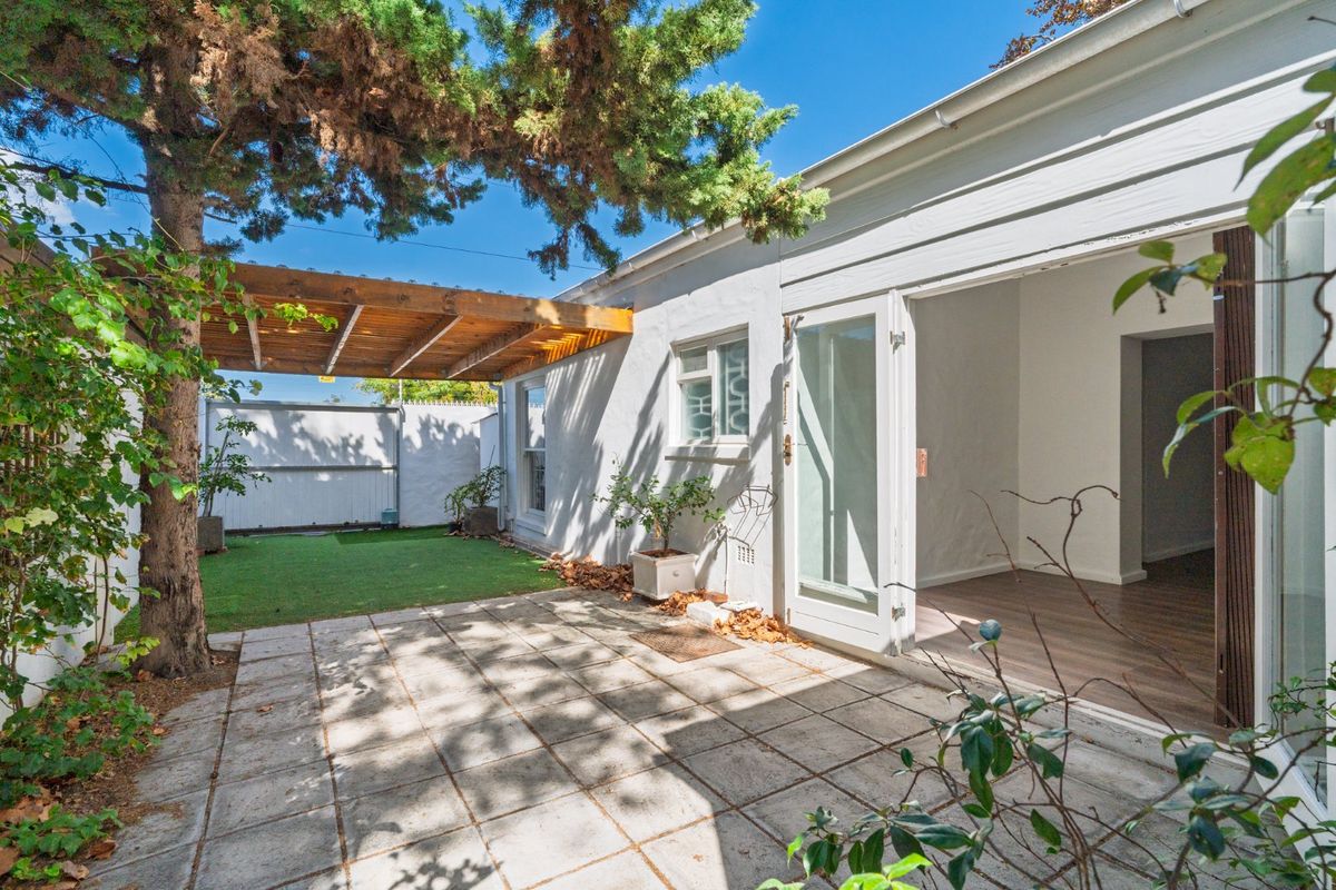 A private rear courtyard featuring a paved patio area, timber pergola, and low-maintenance artificial lawn, accessible via double french doors.