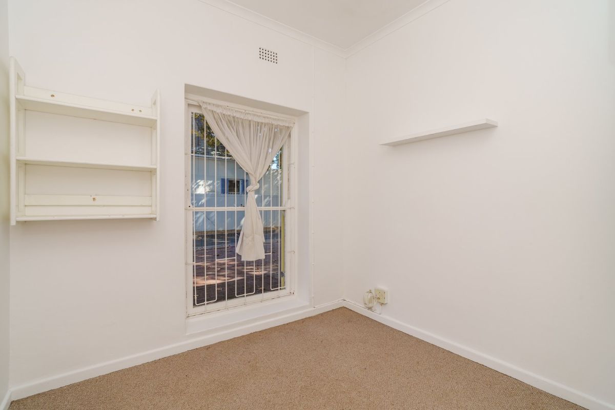 A vacant bedroom featuring neutral walls, carpet flooring, built-in shelving, and a window fitted with a security gate.