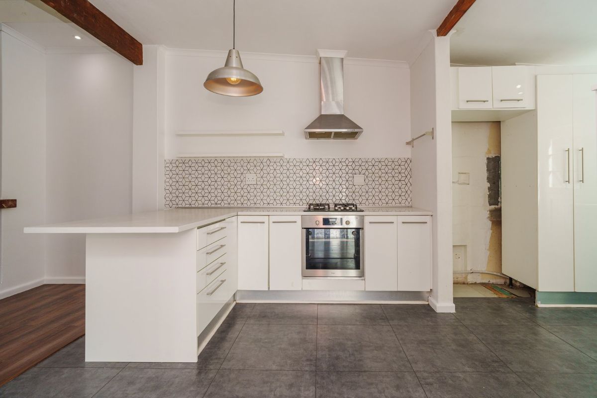 Modern kitchen featuring white cabinetry, stone countertops, geometric tile backsplash, and built-in appliances, with some areas requiring final finishing touches.