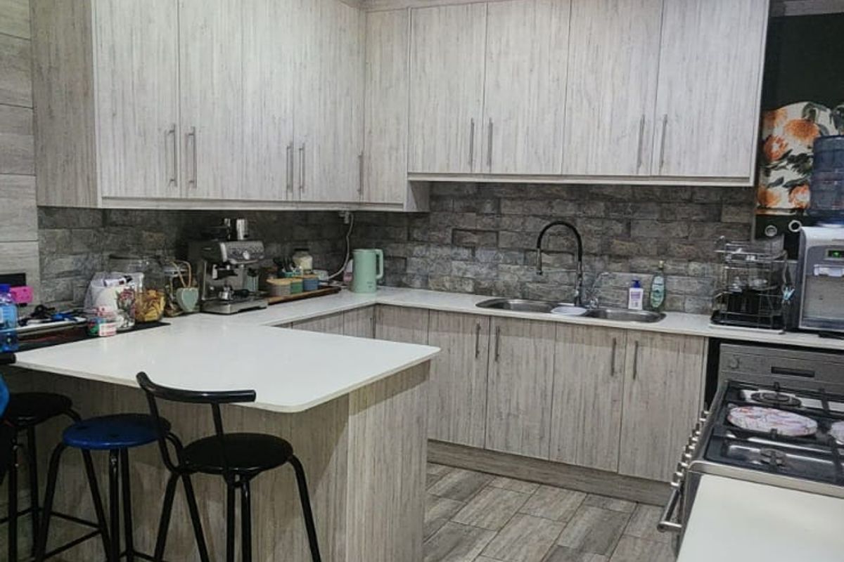 Modern kitchen featuring light wood-grain cabinetry, stone countertops, a stone veneer backsplash, and a breakfast bar island with integrated gas hob.
