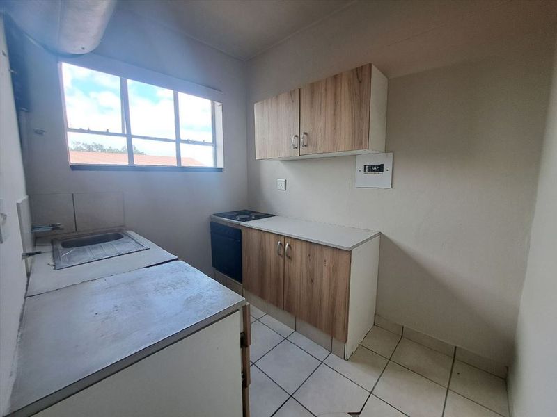 A compact, empty kitchen featuring built-in cabinetry, a stainless steel sink, and a built-in oven with hob, requiring minor cosmetic updates.