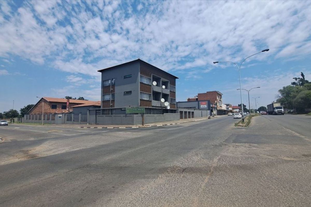 Street level view of a multi-story commercial building situated on a corner lot with perimeter fencing and road access.