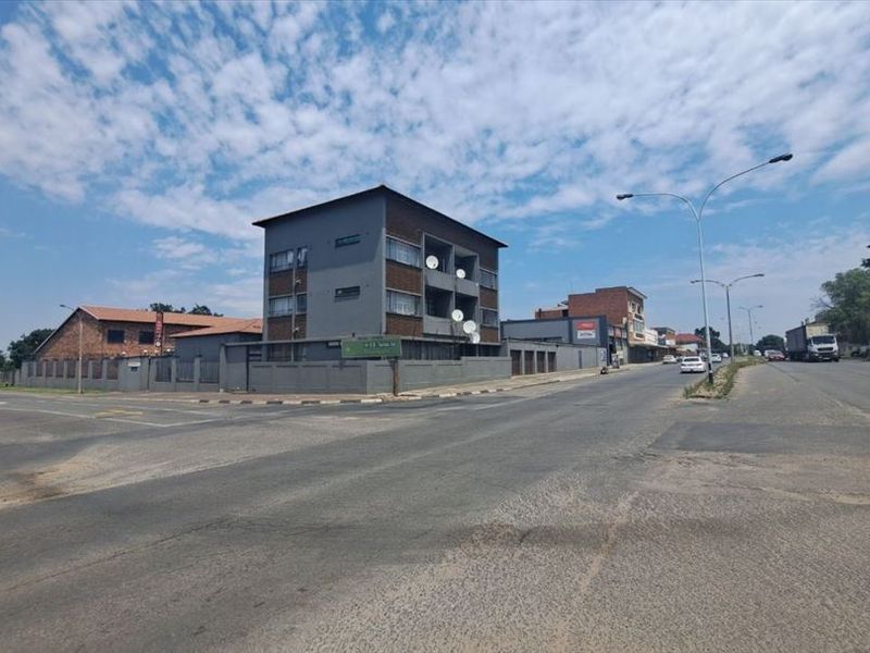 Street level view of a multi-story commercial building situated on a corner lot with perimeter fencing and road access.