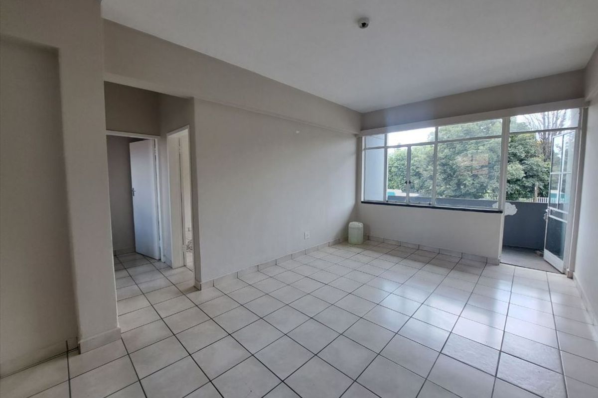 A bright, empty living area featuring neutral tiled flooring, large windows providing natural light, and direct access to an outdoor balcony space.