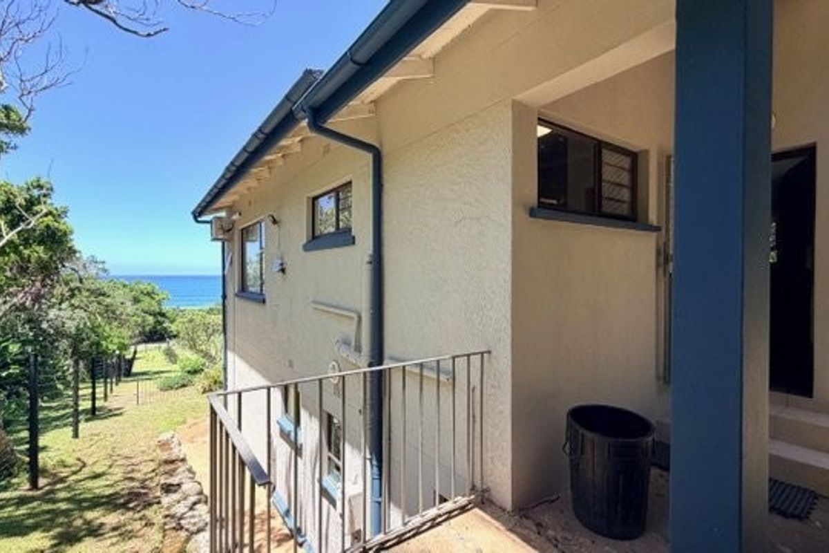 Rear exterior view of the property featuring a metal railing, concrete steps, and a view of the surrounding garden and ocean.