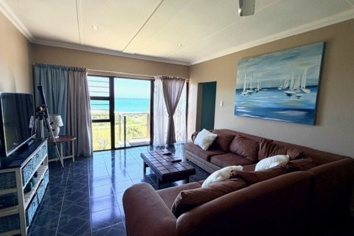 A comfortable living room featuring tiled floors and a large sliding glass door that opens to a scenic coastal view.