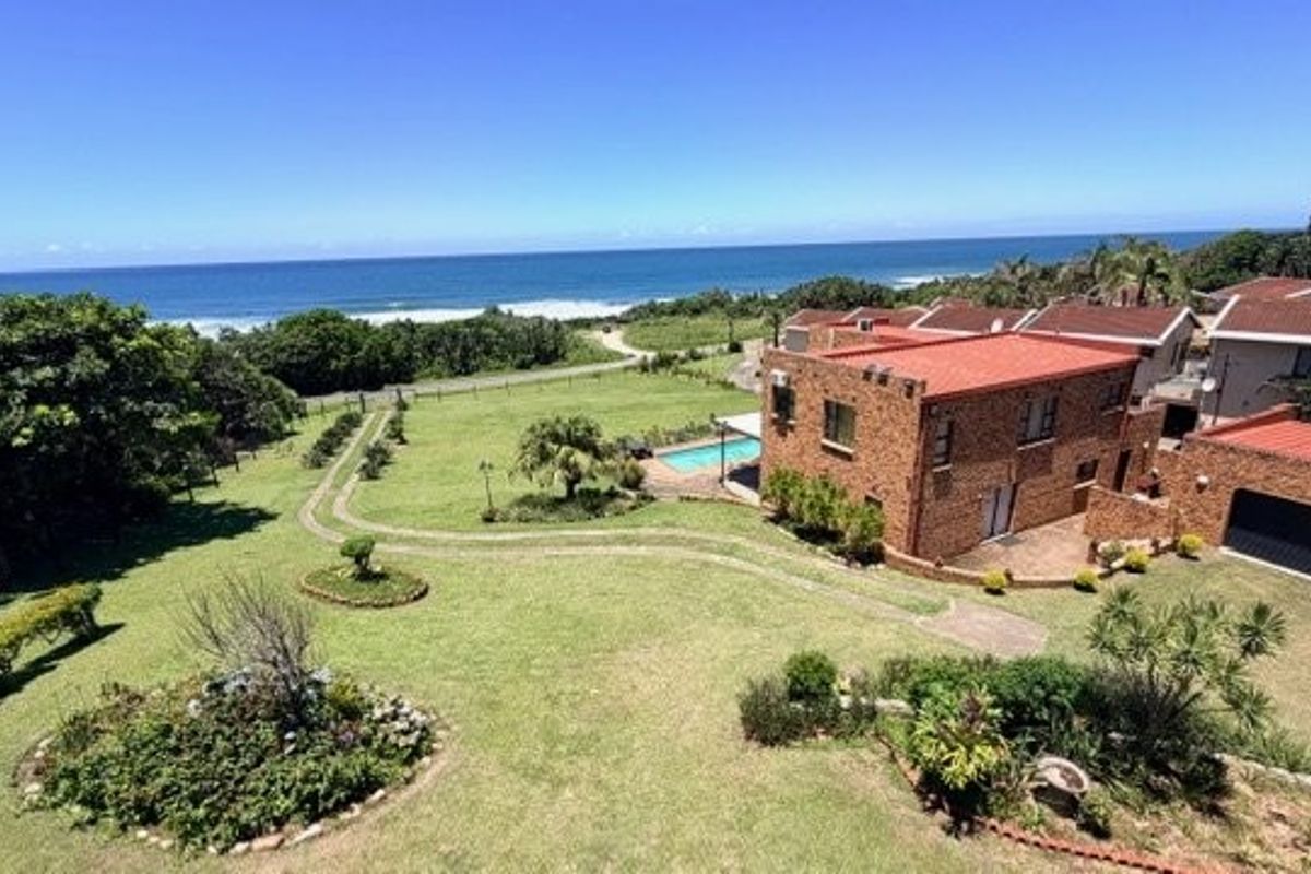 Aerial view of a face brick house with a terracotta roof, swimming pool, and expansive garden, featuring direct ocean views.