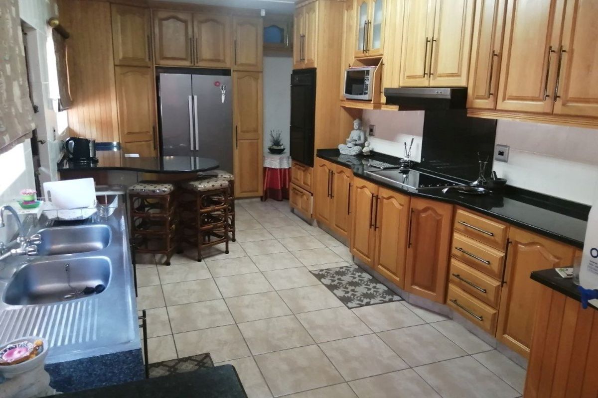 A spacious kitchen featuring extensive wooden cabinetry, granite countertops, a double sink, and integrated appliances including an oven, hob, and extractor fan.