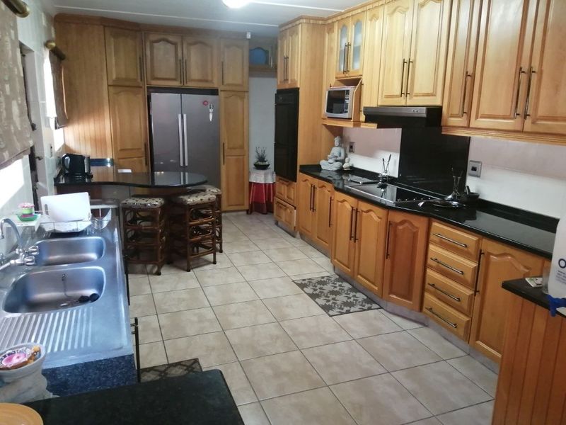 A spacious kitchen featuring extensive wooden cabinetry, granite countertops, a double sink, and integrated appliances including an oven, hob, and extractor fan.