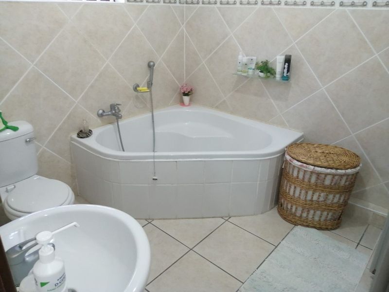 A functional bathroom featuring a corner bathtub, pedestal basin, and toilet with neutral ceramic wall and floor tiling.