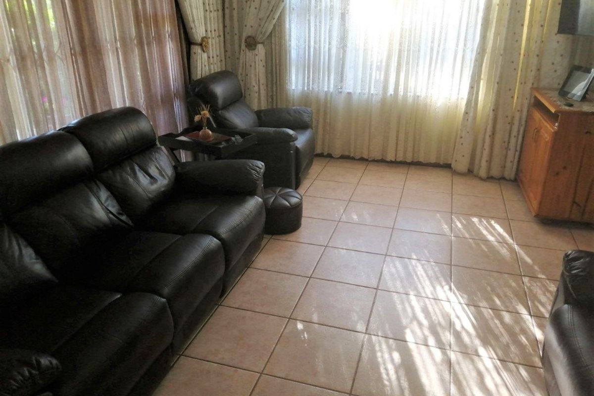 A living room featuring neutral ceramic floor tiles and large windows with curtains, providing a functional and well-lit space.