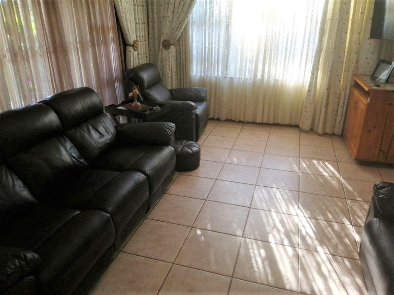 A living room featuring neutral ceramic floor tiles and large windows with curtains, providing a functional and well-lit space.