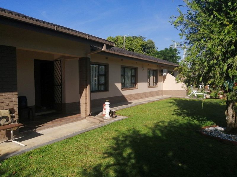 Rear view of the house featuring a covered patio area, well-maintained lawn, and brick exterior walls with secure window frames.