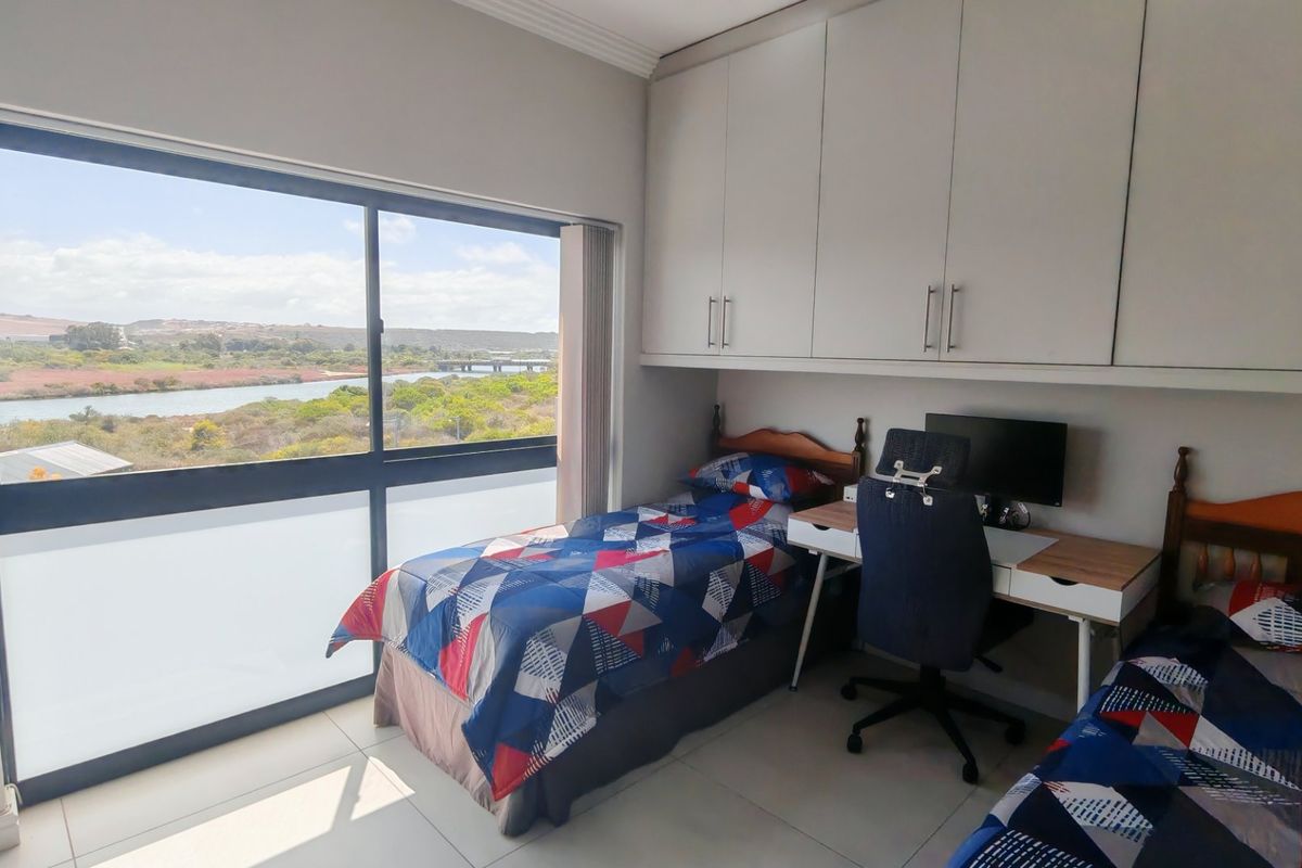 A bright bedroom featuring built-in cupboards, tiled flooring, and a large window offering scenic river and landscape views.