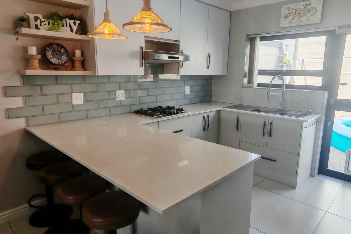 Modern kitchen featuring quartz countertops, subway tile backsplash, gas hob, extractor fan, and ample built-in cabinetry with a breakfast bar area.