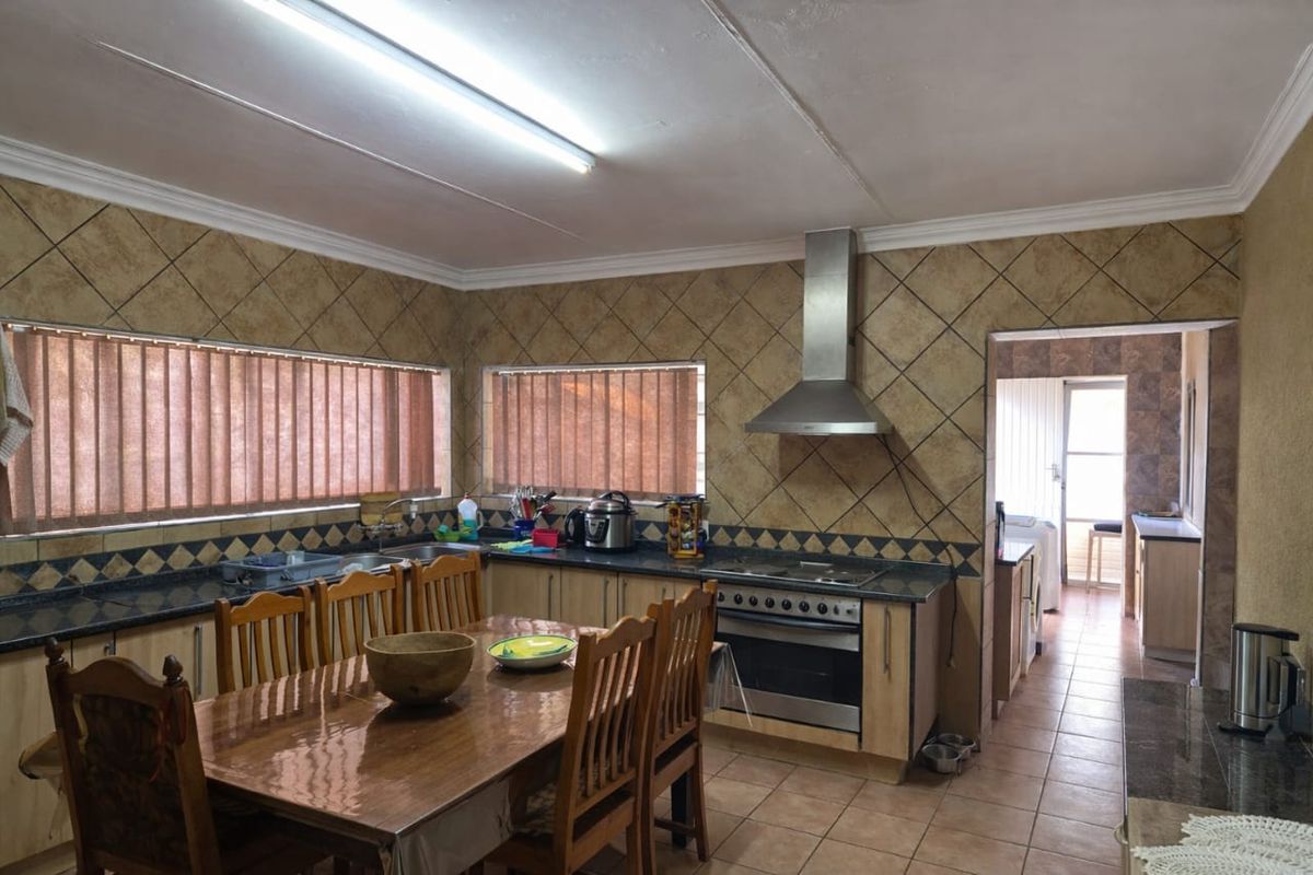 A functional kitchen featuring built-in cabinetry, granite countertops, a stainless steel oven and extractor fan, with a tiled splashback and adjacent scullery area.