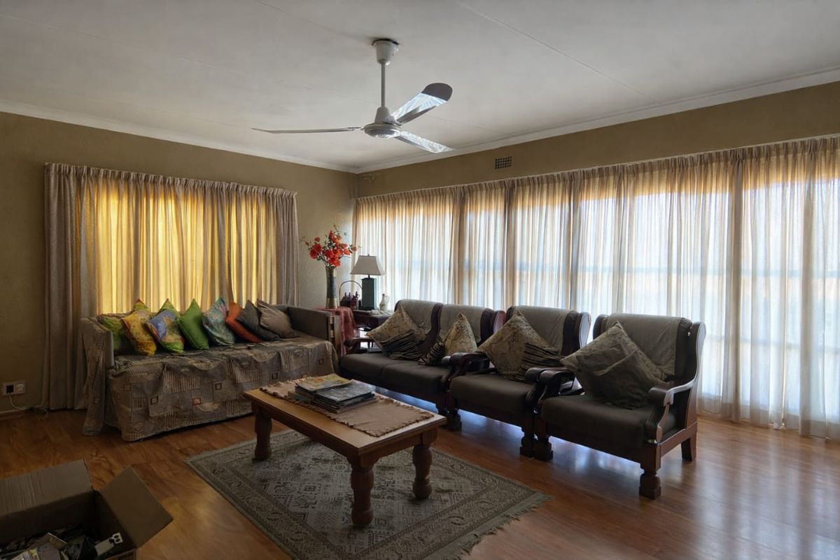 A spacious living room featuring laminate flooring, a ceiling fan, and large windows dressed with floor-to-ceiling curtains, offering a bright and comfortable living space.
