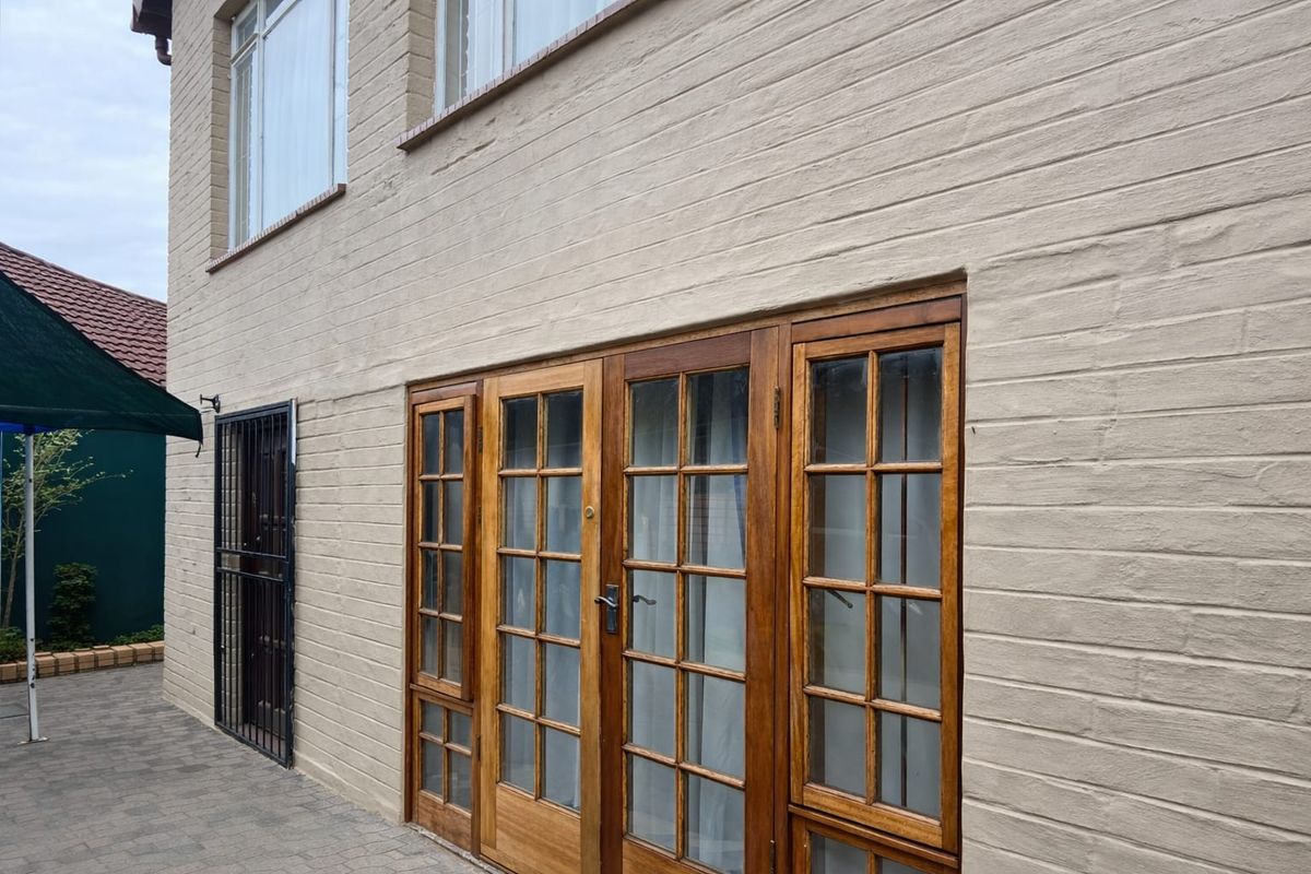 Rear exterior view of the property featuring a painted brick facade, timber-framed french doors, and a paved patio area.