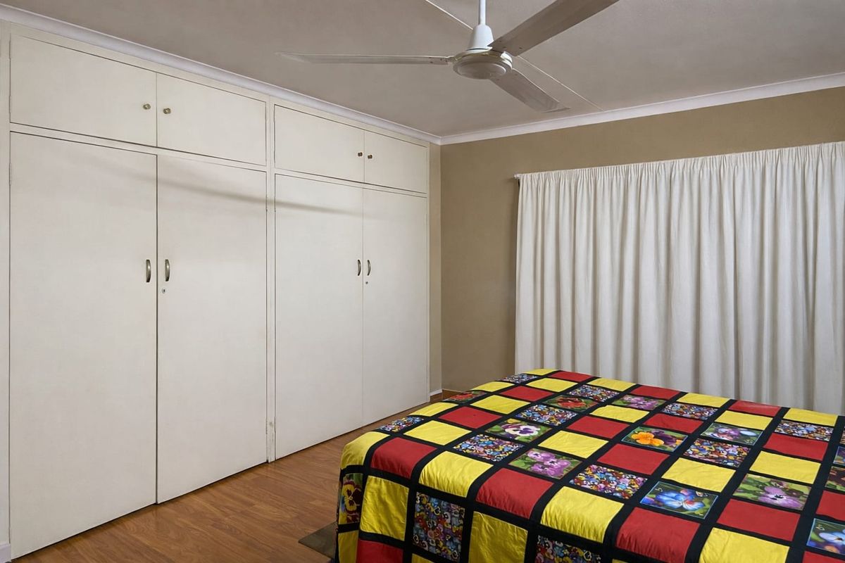 A bedroom featuring extensive built-in storage cupboards, a ceiling fan, and laminate flooring, offering a functional and neutral space.