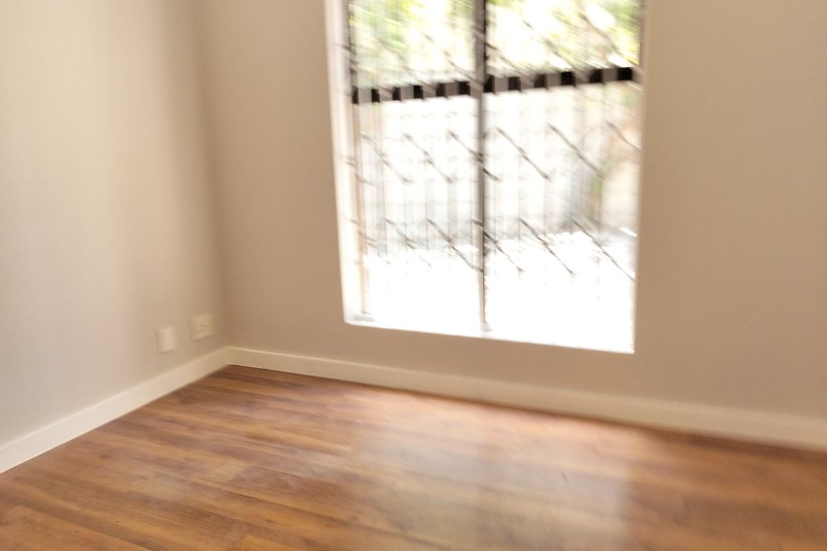 An empty bedroom featuring laminate flooring, neutral walls, and a window fitted with security bars.