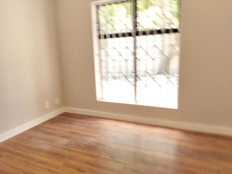 An empty bedroom featuring laminate flooring, neutral walls, and a window fitted with security bars.