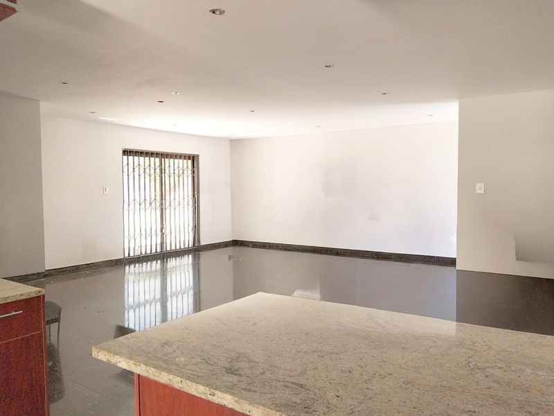 Spacious open-plan living area featuring polished tiled floors, recessed lighting, and a granite-topped kitchen island, leading to a secure exterior access point.