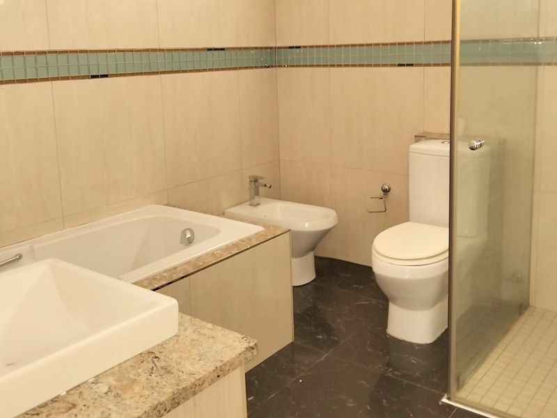 A clean, modern bathroom featuring a built-in bathtub, separate shower enclosure, bidet, and toilet with neutral wall tiling and dark floor tiles.