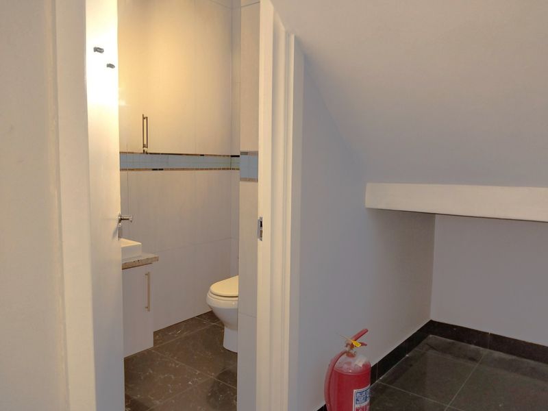 A compact bathroom featuring a modern vanity, basin, and toilet with neutral wall and floor tiling, situated under a sloped ceiling.