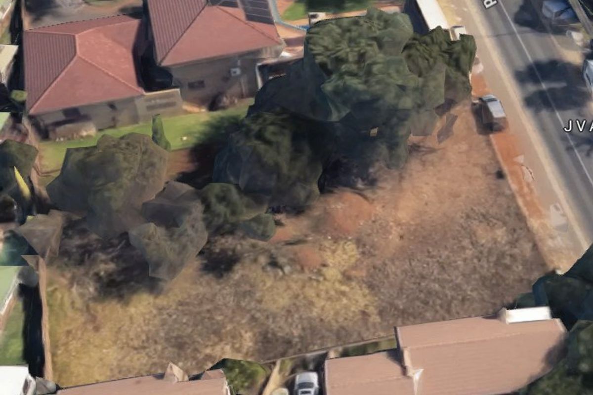 An aerial view of a vacant residential plot showing surrounding neighborhood context and existing boundary lines.
