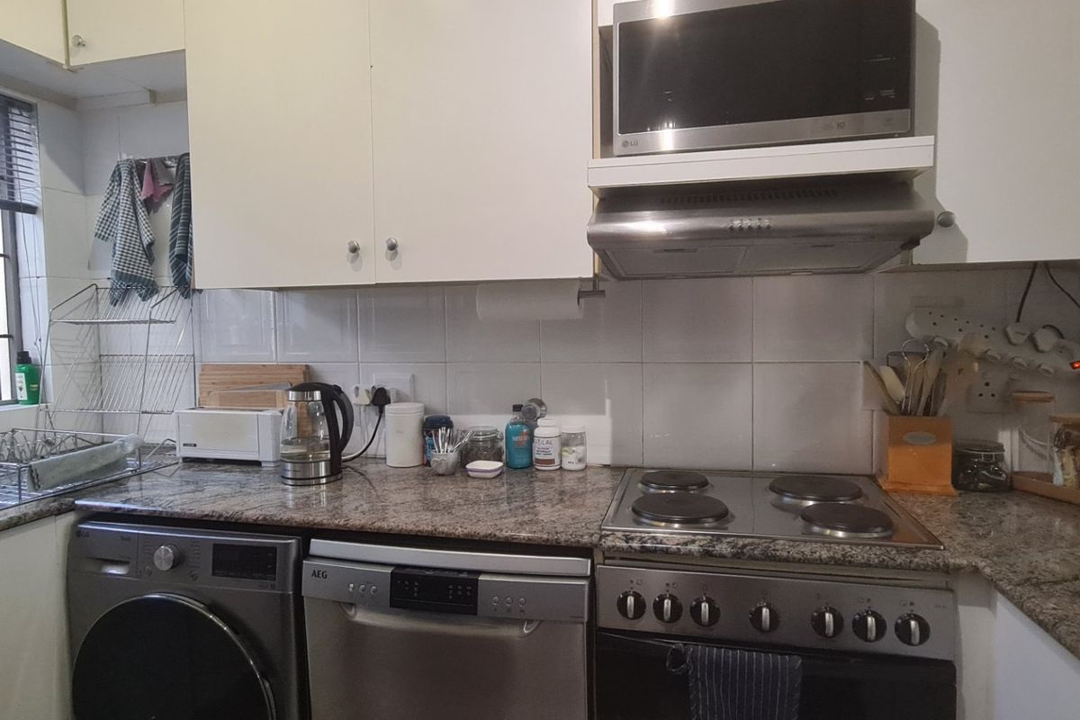 A functional kitchen featuring granite countertops, built-in cabinetry, an electric hob, oven, extractor fan, and integrated microwave with a tiled backsplash.
