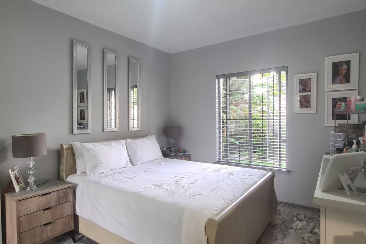 A well-maintained bedroom featuring neutral grey walls, a window with venetian blinds, and ample space for a double bed and storage furniture.