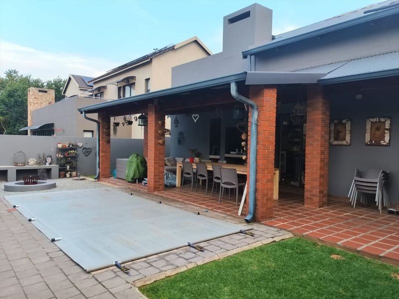 Covered outdoor patio featuring brick pillars, tiled flooring, and a built-in fireplace, overlooking a swimming pool area.
