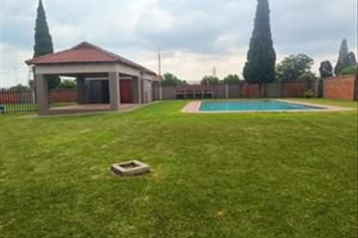 Spacious backyard featuring a swimming pool, a covered patio area, and a well-maintained lawn enclosed by brick boundary walls.