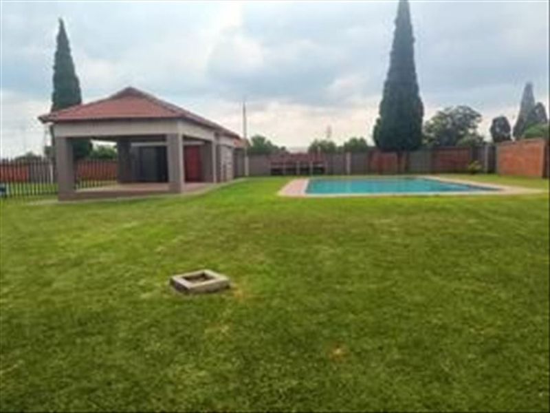 Spacious backyard featuring a swimming pool, a covered patio area, and a well-maintained lawn enclosed by brick boundary walls.