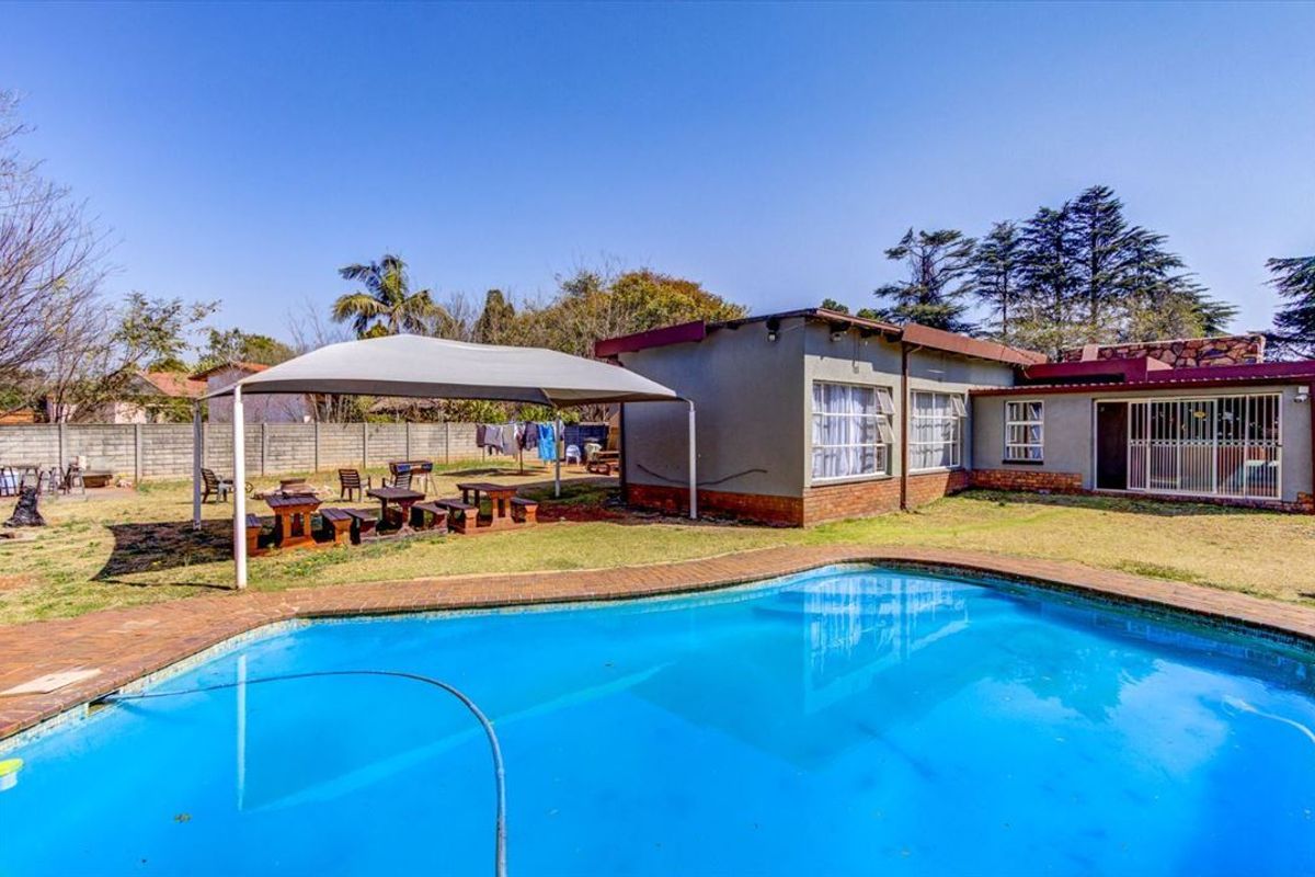 A backyard area featuring a swimming pool with brick coping, a shade sail structure, and a perimeter wall.