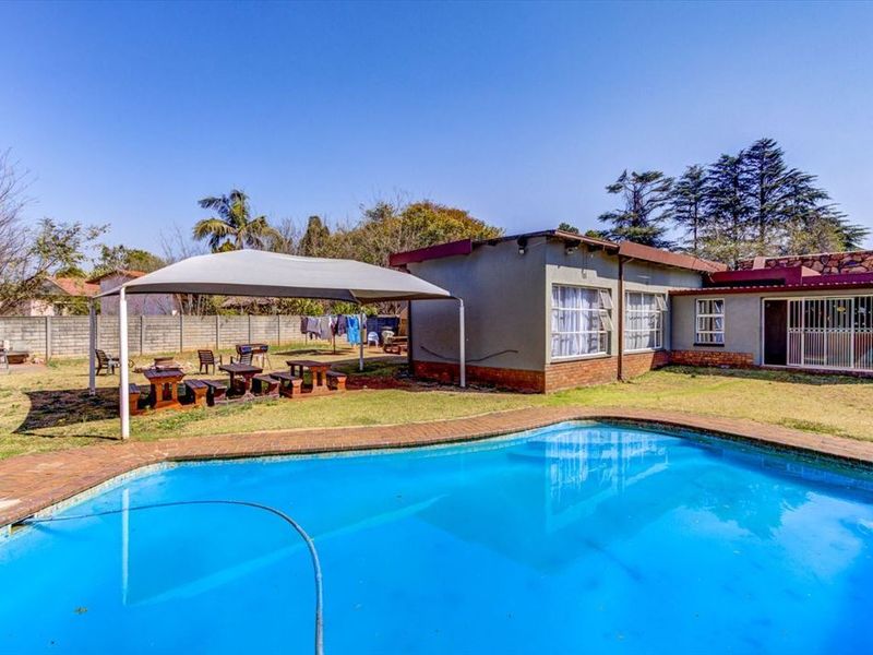 A backyard area featuring a swimming pool with brick coping, a shade sail structure, and a perimeter wall.