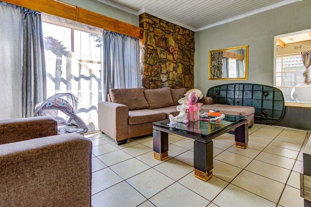A living room featuring a prominent stone feature wall, ceramic tiled flooring, and a timber-accented window frame.