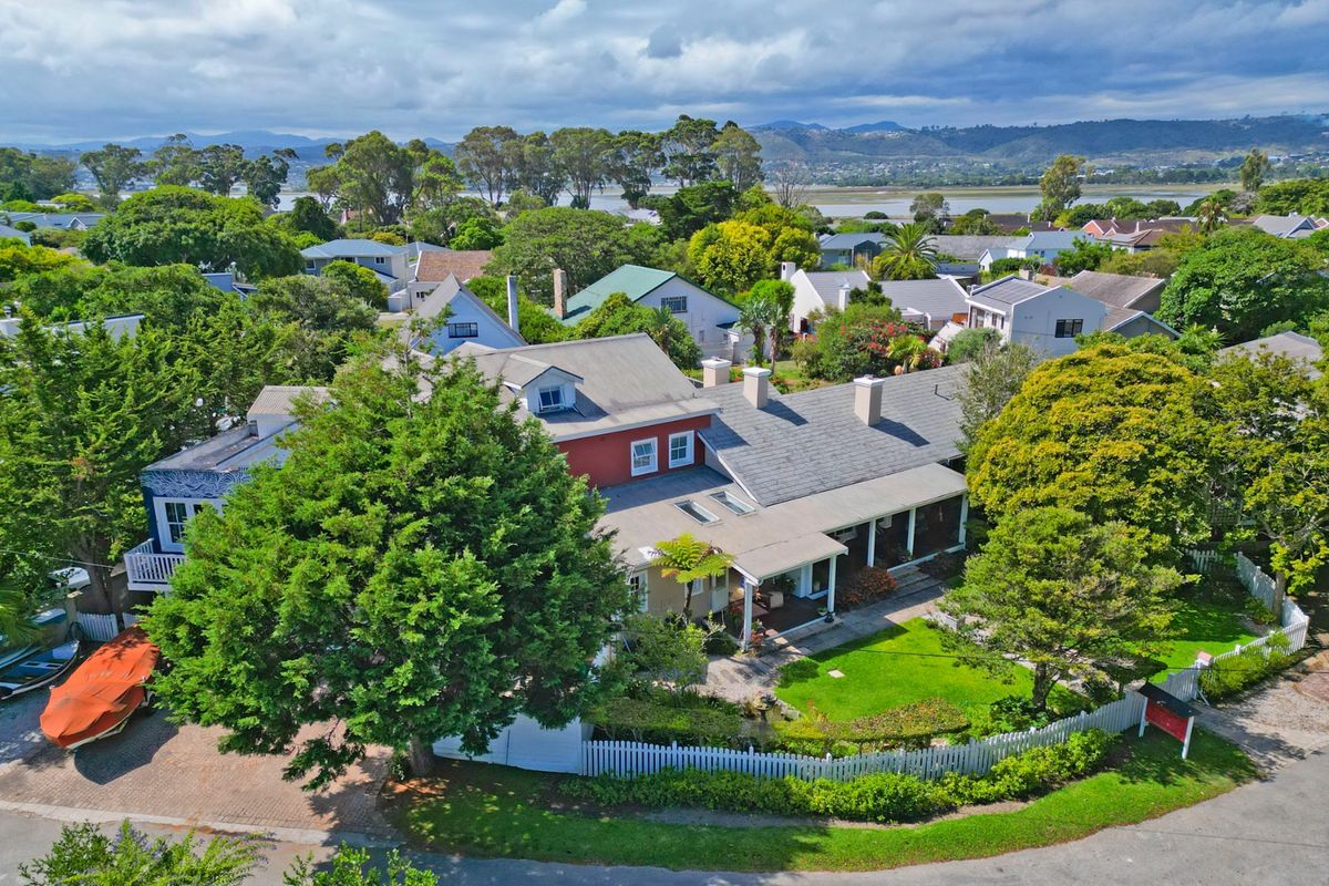 Aerial view of a residential property featuring a pitched roof, covered patio, landscaped garden, and paved driveway in a lush, established neighborhood setting.