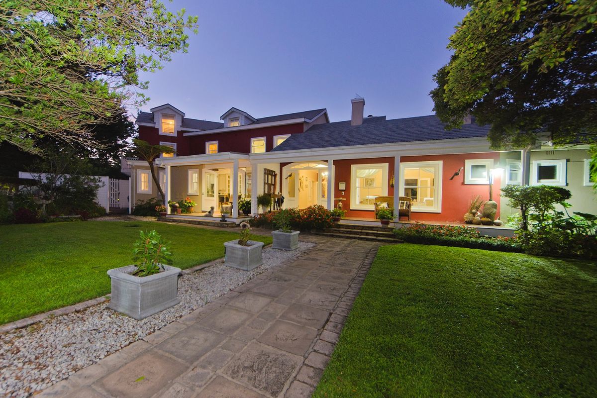 A well-maintained rear exterior view of the house featuring a covered patio, paved walkway, and landscaped garden at dusk.