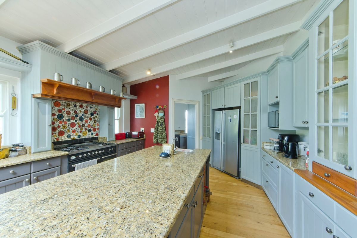Spacious kitchen featuring a large granite-topped island, gas range with mosaic backsplash, custom cabinetry, and exposed beam ceilings with hardwood flooring.
