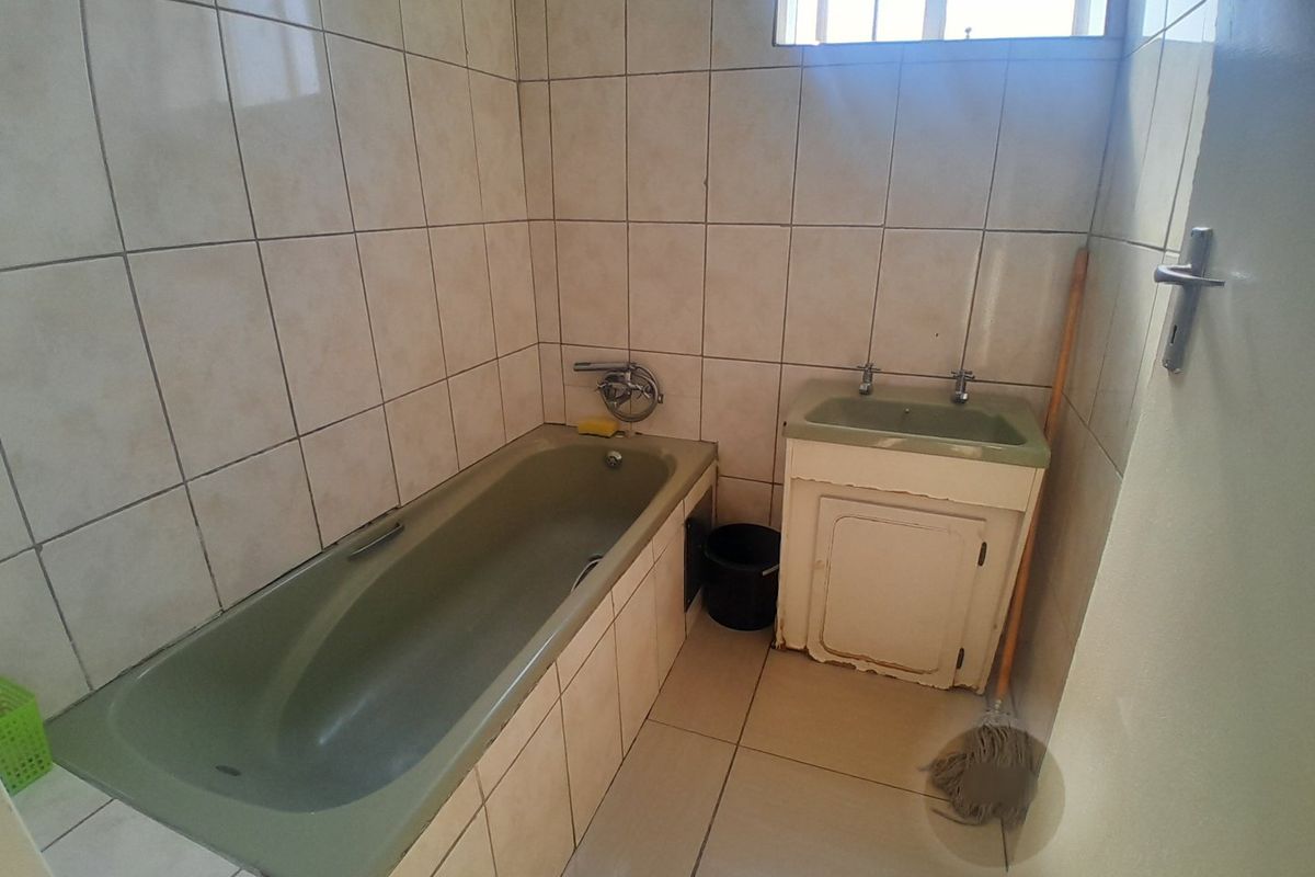 A functional bathroom featuring a built-in bathtub, vanity basin, and tiled finishes, offering potential for modernization and cosmetic updates.