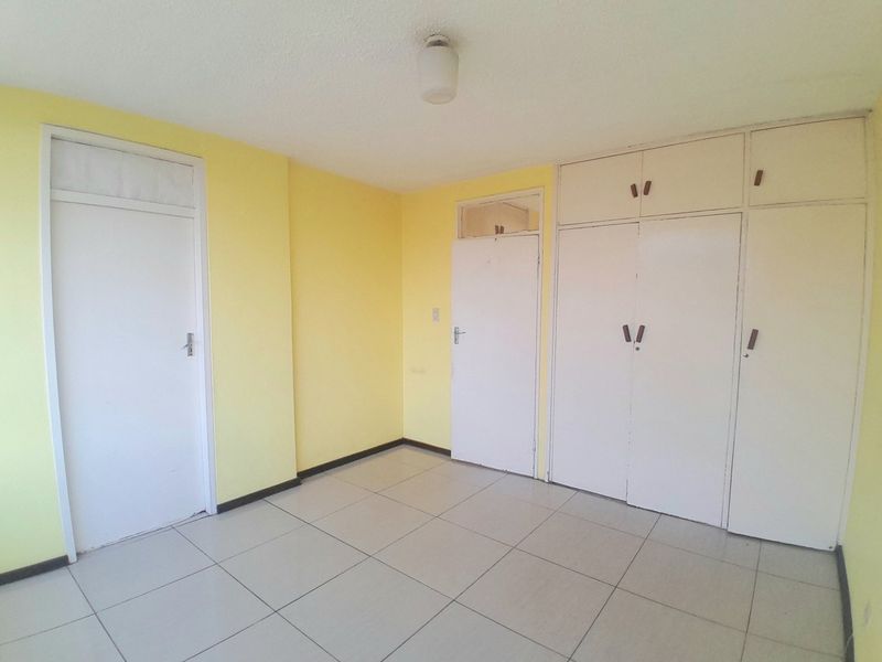 An empty bedroom featuring tiled flooring, built-in cupboards, and yellow painted walls, offering a blank canvas for personalization.