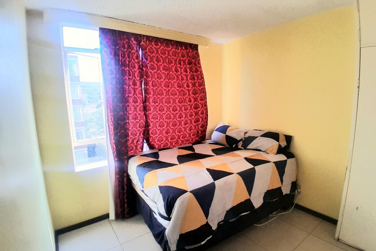 A compact bedroom featuring tiled flooring, a built-in wardrobe, and a large window providing natural light.