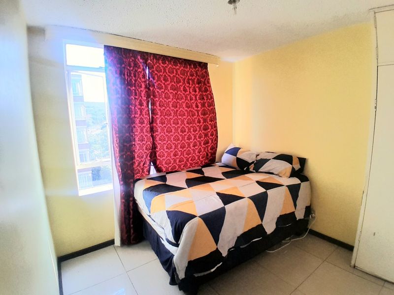 A compact bedroom featuring tiled flooring, a built-in wardrobe, and a large window providing natural light.
