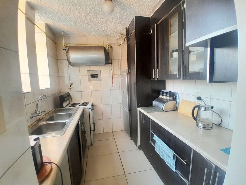 A functional galley-style kitchen featuring dark cabinetry, tiled surfaces, and a double basin sink, offering potential for modern updates.