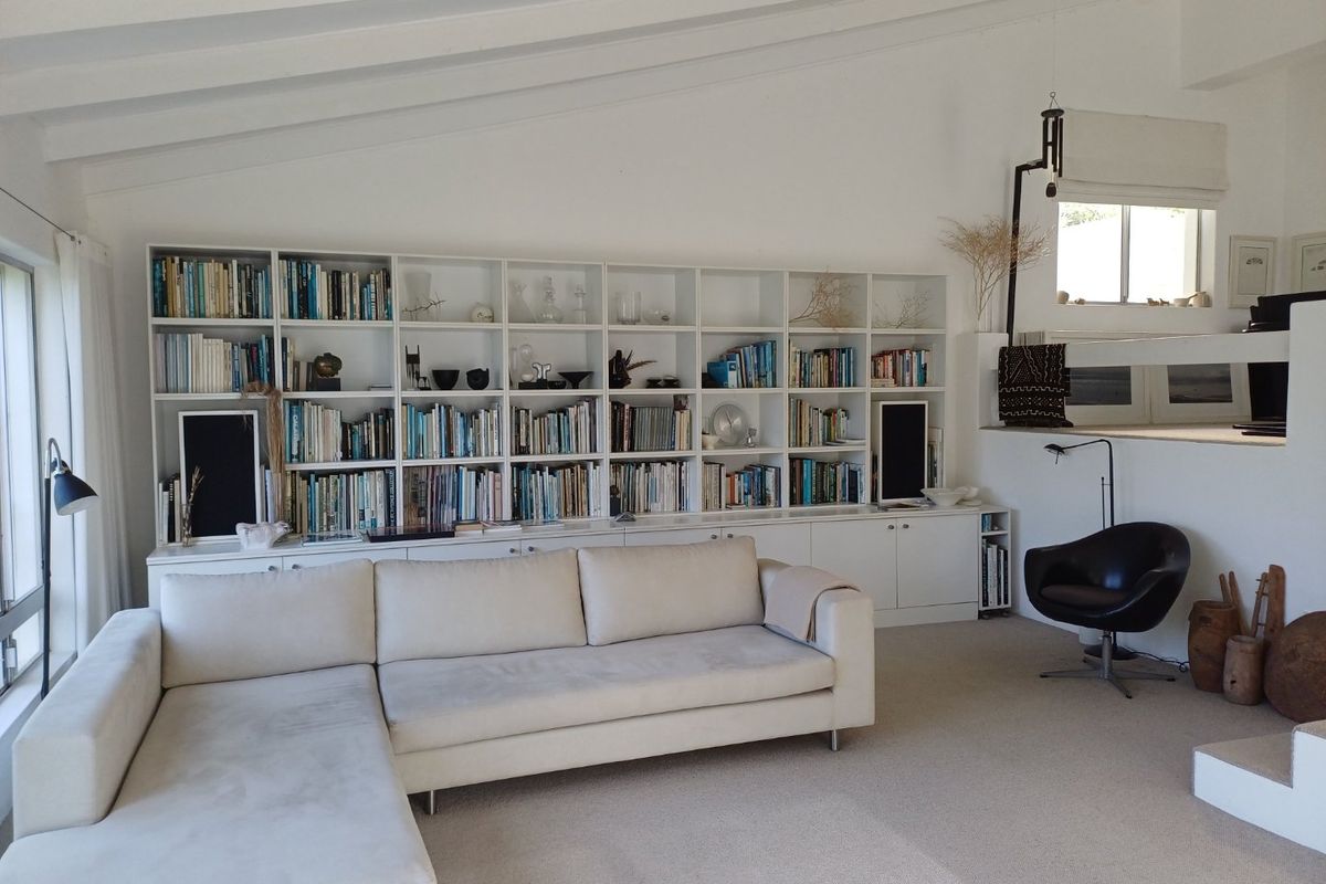 A bright living room featuring a large built-in floor-to-ceiling bookshelf, vaulted ceilings, and neutral carpeting.