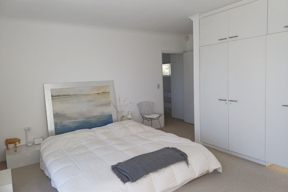 A bright bedroom featuring neutral carpeted flooring, white walls, and extensive built-in storage cupboards with a clean, minimalist aesthetic.