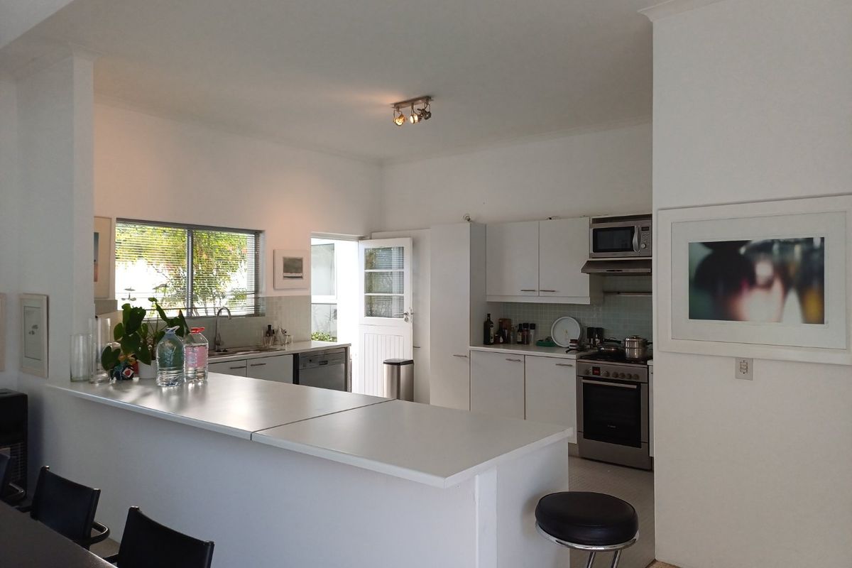 A functional kitchen featuring white cabinetry, a central island, stainless steel appliances, and a tiled splashback, offering a clean and practical layout.