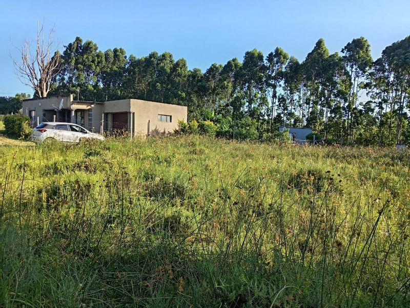 A view of a residential property featuring a structure with a garage, set on a large plot of land with overgrown grass.